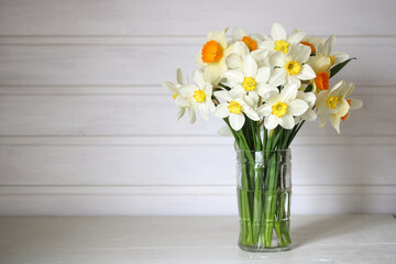 daffodils of different varieties in a glass mug on a white table in a cottage interior. spring flowers.