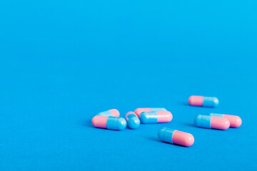Heap of pink and blue pills on colored background. Tablets scattered on a table. Pile of red soft gelatin capsule. Vitamins and dietary supplements concept