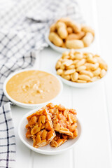 Sweet peanut brittle, peanuts and peanuts butter on white table.