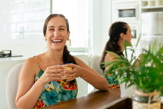 happy woman smiling and drinking coffee at living room table