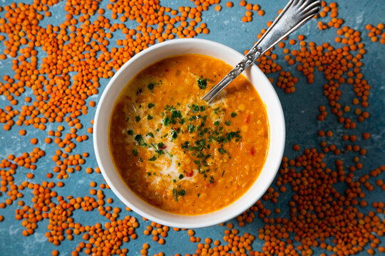 Top view of a bowl of red lentil soup surrounded by uncooked lentils