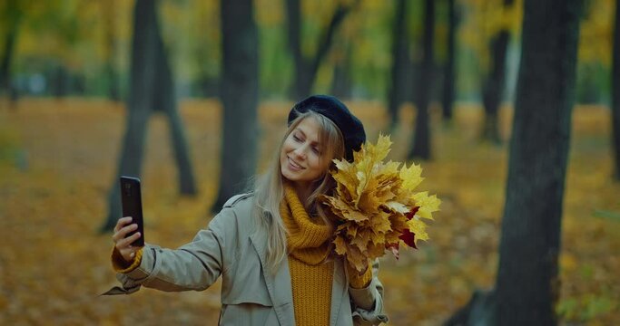 young woman taking photo of her face by camera of mobile phone in beautiful autumn park, 4K, Prores
