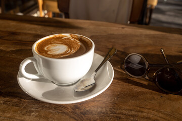 A cup of latte coffee with a heart in a white mug with a spoon on a wooden table in a restaurant
