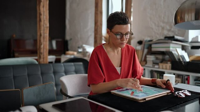 Concentrated female architect with short hair in eyeglasses working on tablet in the office