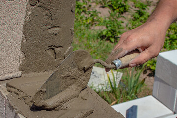 A bricklayer using a trowel lays a layer of mortar on the surface of a white foam block EPS wall under construction. outdoor construction scene