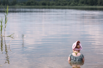 A little girl of three years old bathes in a forest lake in the summer.