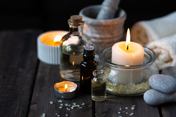 Spa setting with essential oil, candle, sea salt, pebbles, towel on dark wooden background. Massage, aromatherapy. Natural organic ingredients for relaxation, detention. Wellness in salon concept