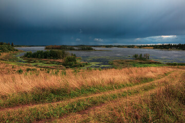Fototapeta na wymiar Landscape of a lake in a field, storm clouds, dirt road.