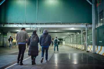 Two men and a woman dressed in winter clothing walking toward a covered pedestrian walkway, jackets, hats, backpacks
