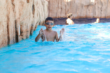 Young boy kid child six years old splashing in swimming pool having fun leisure activity wearing sea glasses practicing swimming