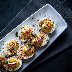 Deviled eggs garnished with smoked paprika , sliced radish , and chopped basil.