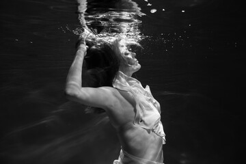Young beautifull caucasian woman in dress under water in black and white