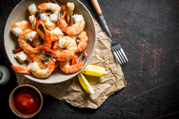 Cooked shrimps in a bowl on paper with sauce and lemon slices.
