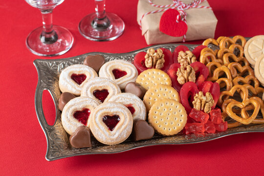 Valentine's Day Plate with shortbread, chocolate hearts, crackers, red candies and walnuts on red background
