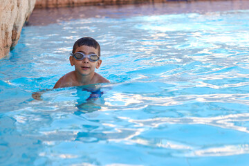 Young boy kid child six years old splashing in swimming pool having fun leisure activity wearing sea glasses practicing swimming