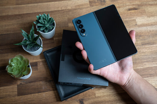 Budapest, Hungary - January 05, 2023. Samsung Galaxy Z Fold 4 in gray-green color. The device in the open position in the hands of a man. A wooden table in the background.