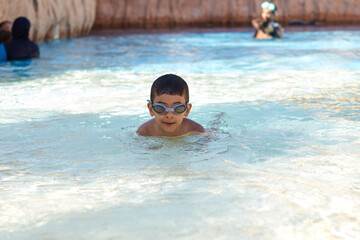 Young boy kid child six years old splashing in swimming pool having fun leisure activity wearing sea glasses practicing swimming