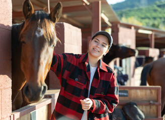 Caring young female farmworker petting stroking head of horse on animal ranch club on autumn sunny...