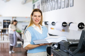 Cheerful woman printing shop manager holding ream of paper and looking at camera.