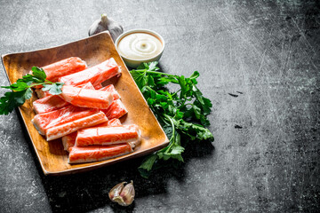 Crab sticks on a wooden plate with greens and sauce. © Artem Shadrin