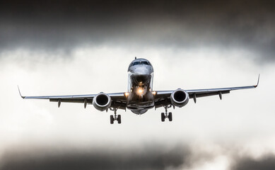 Between dark clouds, front view of a plane during the approach phase, about to land. 