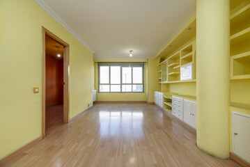 Fototapeta premium Living room of a house with a wall lined with a yellow painted plaster bookcase, a glass cabinet with glass doors and white lacquered wooden base units