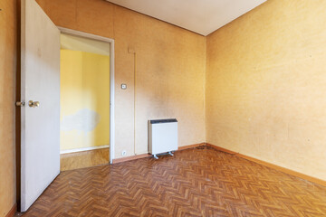 Empty and old room with wood-like sintasol floors, electric heat accumulator radiator and papered walls