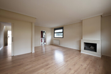 Living room of an empty house with chestnut floor, entrance to the hall, fitted kitchen and fireplace