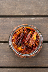 A clear glass jar without a lid full of dried chillies on an acacia wood surface viewed from the top
