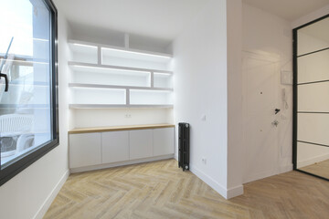 Living room of a new empty house with a white access door and a bookcase with plaster shelves and wooden base units