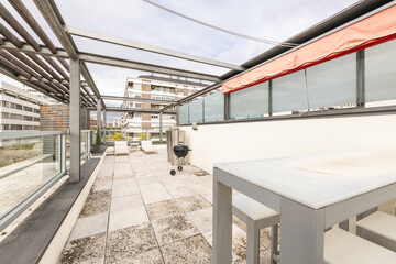 Terrace on the attic floor of a building with retractable awnings and metal tables and white Teflon...