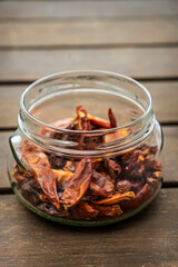 A clear glass jar filled with dehydrated hot hot dried chillies on acacia wood surface