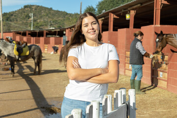 Portrait of young female stable visitor smiling at camera in horse club on sunny spring day
