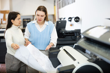 Female printing office workers discussing printed large format scheme or map.