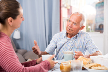 Fototapeta na wymiar Elderly father and adult daughter talk and drink tea in the kitchen. High quality photo