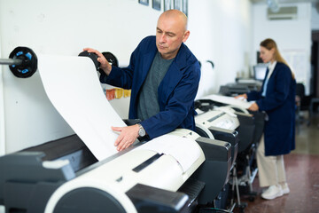 Obraz premium Service man uses plotter and checks the functionality in printing shop