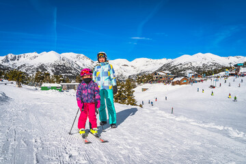 Mother and daughter, family, on ski, standing and smiling, ski resort, snow capped mountains and...