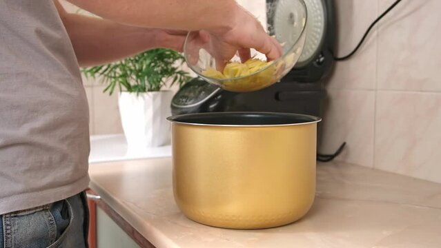 The man puts the potatoes cut into thin slices into bowl of slow cooker. multicooker. Cooking lunch dinner for family at home. The process of cooking meat in French with potatoes, tomatoes, cheese.