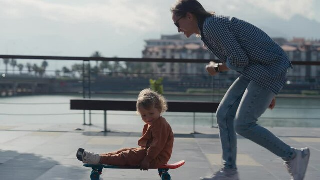 Mother pushing little son sitting on skateboard