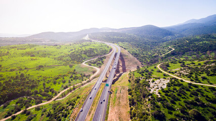Aerial view shot flying over green hills fields, presents highway road and modern bridge with...