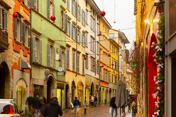 Fototapeta na wymiar View of typical narrow cobbled street of historical Italian city of Bergamo with colorful buildings and traditional Christmas decorations during winter holidays