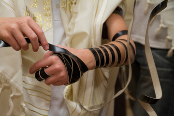 An young man wrapping Jewish Tefillin on his arm and wearing prayer shawl for praying. Preparing...