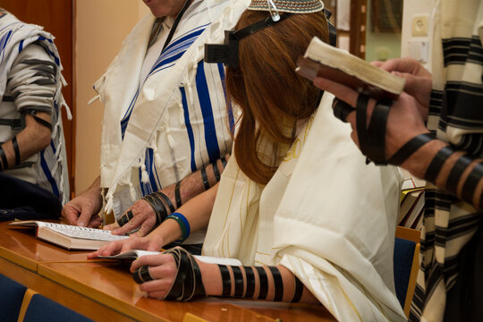 A praying young man with a tefillin on his arm and head, holding a bible book, while reading a pray at a Jewish ritual (Bar Mitzvah ceremony)