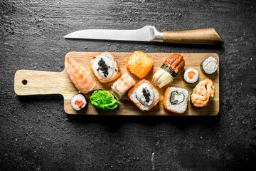 Sushi rolls with shrimp, vegetables and salmon on a cutting Board with a knife.