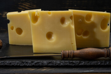 Block of Swiss medium-hard yellow cheese emmental or emmentaler with round holes and cheese knife