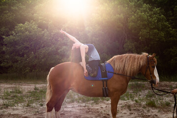 young woman doing yoga on a horse against the backdrop of trees