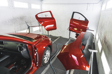 A luxury red car in a paint shop with its doors removed for a fresh coat of paint. High-quality photo