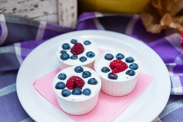 Three servings of yogurt dessert with fresh raspberries and blueberries in a ceramic ramekin