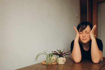 tired mom alone in the kitchen with a headache sitting at the table in silence