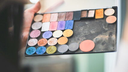 The makeup artist is holding a palette of shadows.